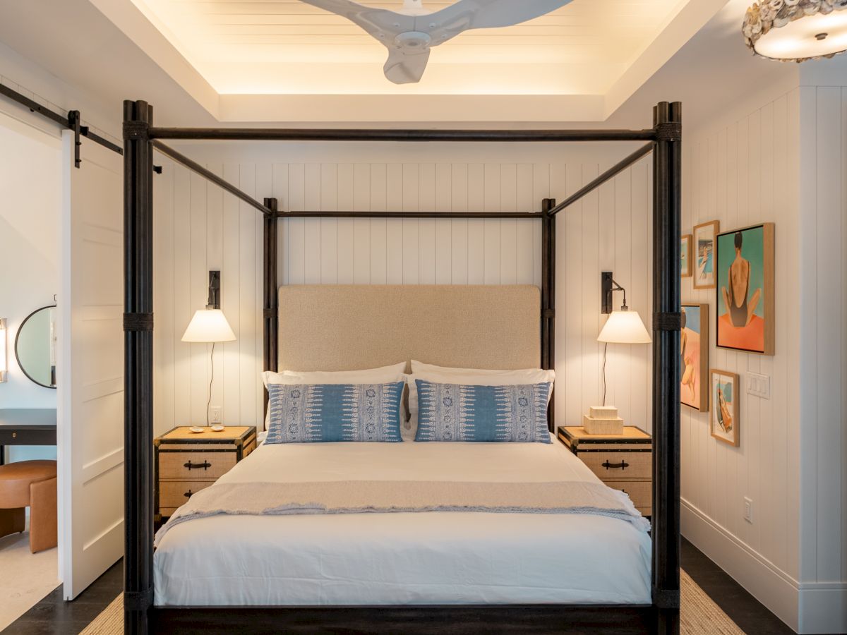 A luxurious four-poster bed with dark wood frame, white linens, blue accent pillows, matching nightstands, lamps, and framed art on the wall.