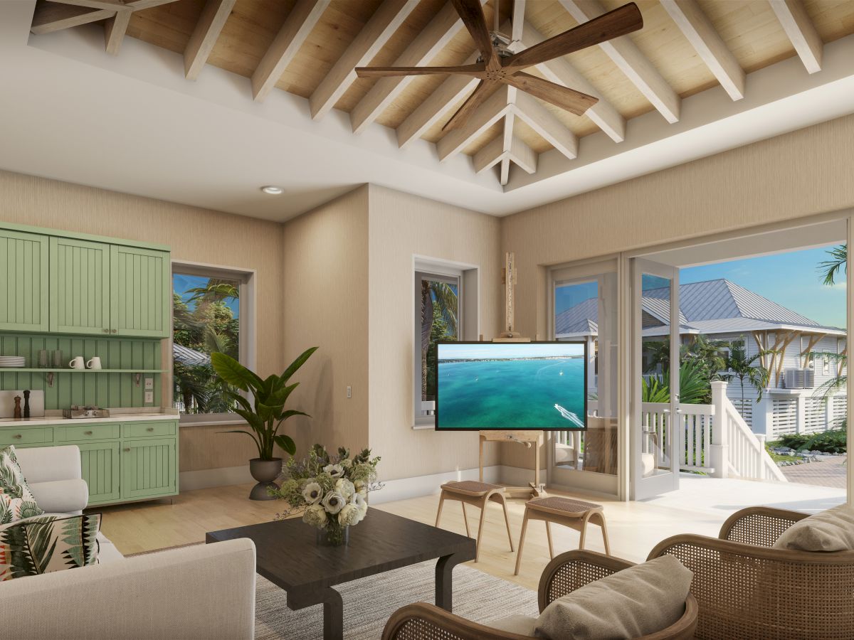 A bright, airy living space with a mint-green kitchen, wicker seating, a coffee table, a wall-mounted TV, ceiling fans, and large glass doors opening to an outdoor deck.