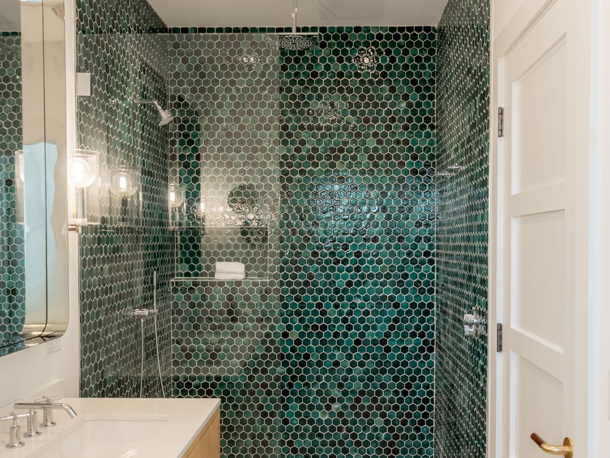 A modern bathroom with a glass-enclosed shower featuring dark teal hex tile, white vanity, and soft lighting, stylish and bright.