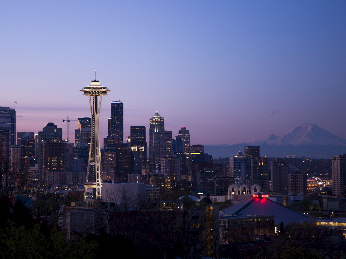 Seattle skyline at dusk, featuring the Space Needle and distant Mount Rainier under a colorful sky.