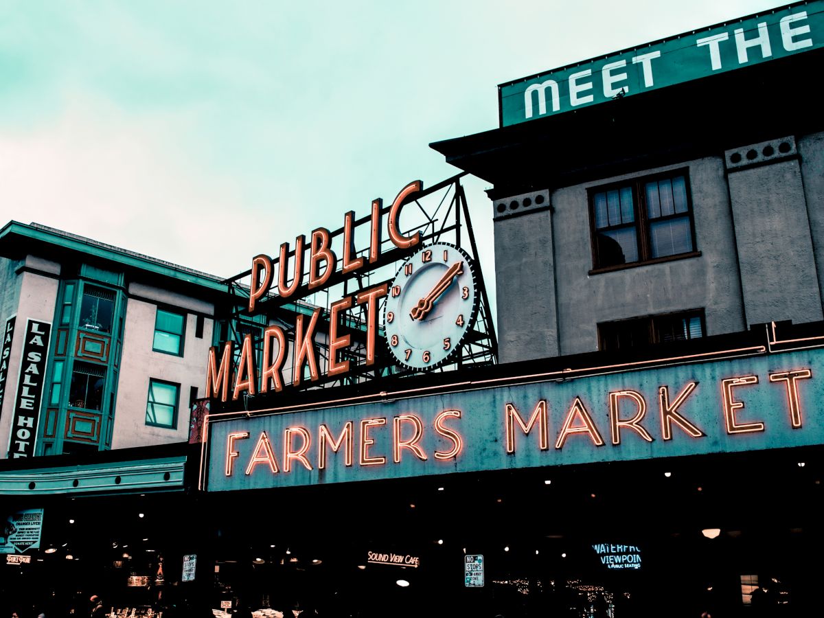 A neon sign reading "Public Market" and "Farmers Market" on a building, indicating a lively shopping area.